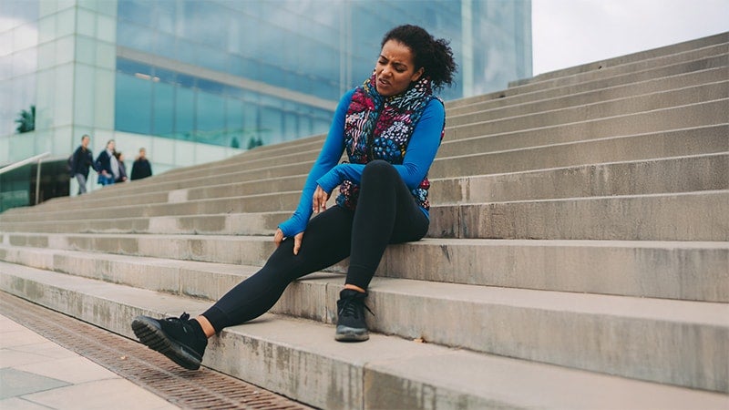 Woman on concrete steps massaging her legs and indicating pain in joints.