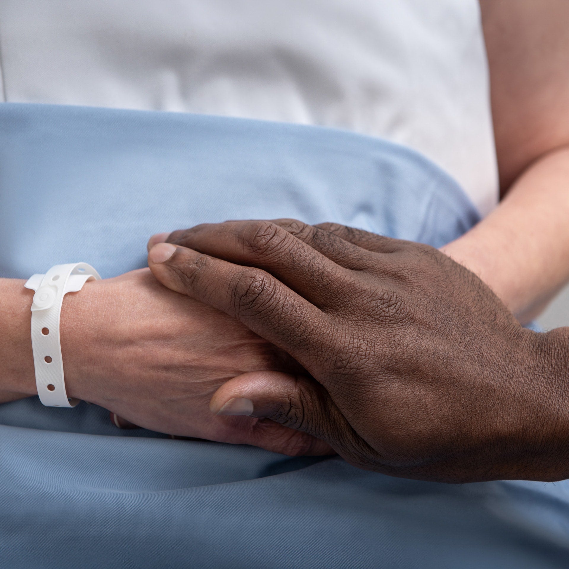 Close-up image of a clinician's hand placed over a patient’s hands.