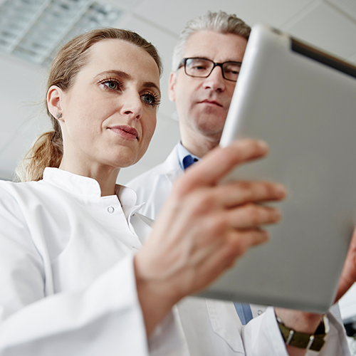 Two people in lab coats looking at a tablet