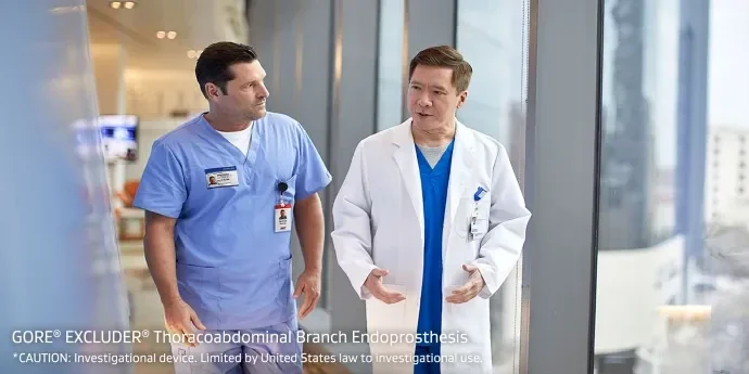 Doctors converse while walking in hallway.