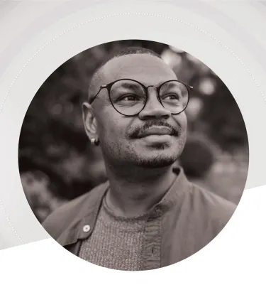 Black-and-white portrait of a person wearing round glasses and a jacket, looking slightly upward and to the side with a calm, thoughtful expression, framed within a circular design on a light abstract background.