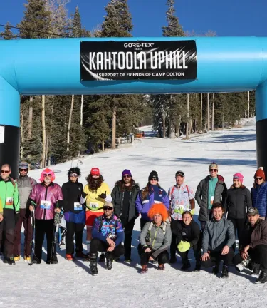 Group of participants in winter gear posing beneath a GORE-TEX Kahtoola Uphill event arch on a snowy ski slope.