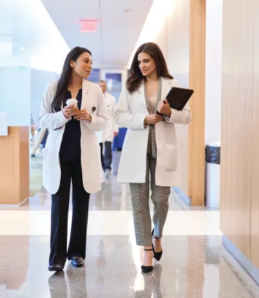 Two female health care professionals walking down a hallway together and talking