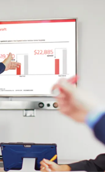 A presenter points to a screen displaying vascular graft data in a meeting room
