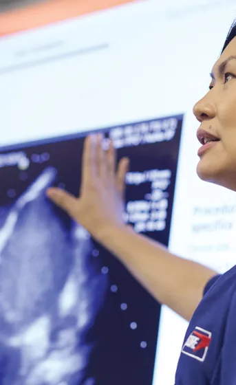 close up of woman in blue scrubs presenting case information on large screen