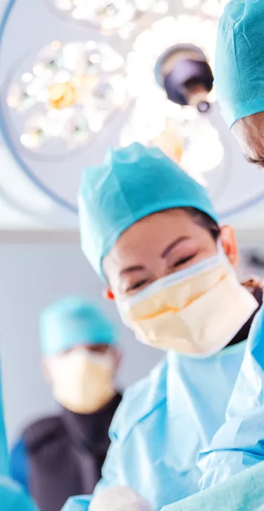 view of three doctors in blue scrubs looking down at a patient in an operating room